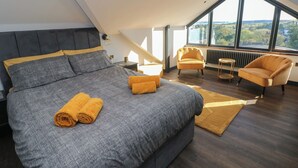A modern bedroom with a large bed, two armchairs, and a view of the outdoors. - 10 Brython Place (Tenby)