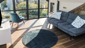 A modern living room with a large skylight, a grey sofa with patterned cushions, a blue armchair, and a round rug. - 10 Brython Place (Tenby)