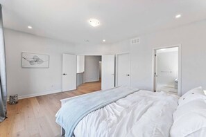 Une chambre avec un grand lit, des murs blancs et un plancher en bois. Deux portes donnent accès à d’autres pièces.