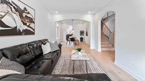 Ett modernt vardagsrum med en svart lädersoffa, ett soffbord i marmor och en stor, abstrakt målning. En trappa syns till höger.