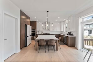 A modern kitchen with a central island, white cabinetry, and a dining area with four chairs. - *NEW* Prestigious 5BED Home | 25MINS 2DT (Ottawa)
