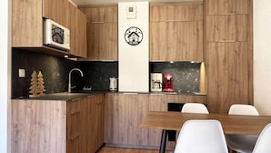 Una cocina compacta con armarios de madera, encimera negra, logotipo blanco montado en la pared y una mesa de comedor con sillas blancas.