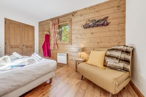 A wooden-paneled room with a bed, a sofa, a window with curtains, and a wall-mounted shoe rack.