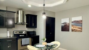 A modern kitchen with dark cabinets, a stainless steel stove, and a dining area with a glass table and two chairs.