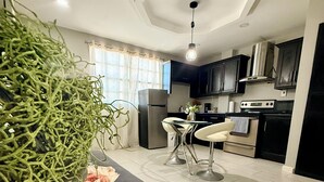A modern kitchen with a central island, black cabinets, stainless steel appliances, and a large potted plant.