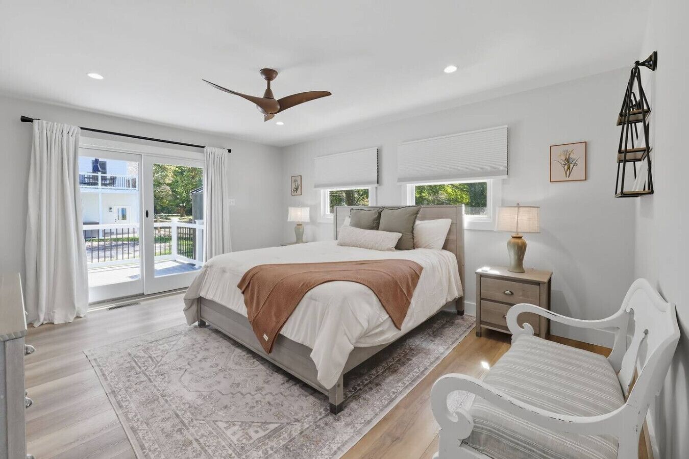 Une chambre avec un lit, des tables de chevet, une chaise, un ventilateur de plafond et une vue sur l’extérieur, accessible par une porte coulissante.