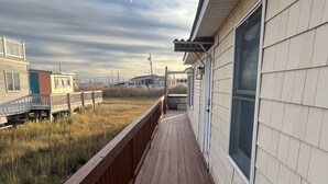 A wooden deck leading to a house with a large window, surrounded by a grassy area and other houses in the background. - Back Bay Getaway (Wildwood)