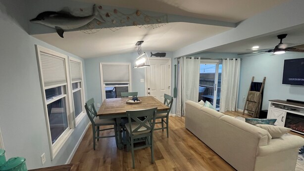 A dining area with a wooden table and chairs, a sofa, and a television in the living room. - Back Bay Getaway (Wildwood)