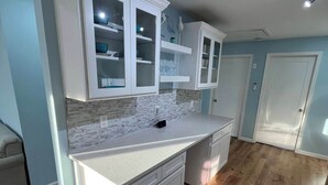 A modern kitchen with white cabinetry, a marble countertop, and wooden flooring. - Back Bay Getaway (Wildwood)