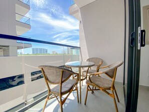A balcony with wicker chairs and a glass table, overlooking a cityscape.