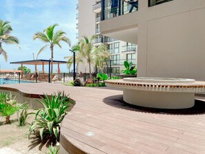 A rooftop pool area with a circular seating area, surrounded by potted plants and palm trees.