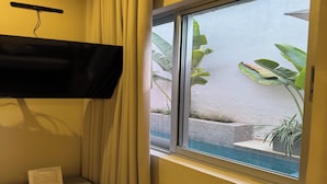 A room with a TV mounted on the wall, a window with a view of a pool and plants, and a sign on the floor. - Cómoda habitación Twin en Manga cerca al Centro (Cartagena)