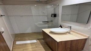 Un baño moderno con cabina de ducha de vidrio, tocador de madera con lavamanos y un espejo grande.