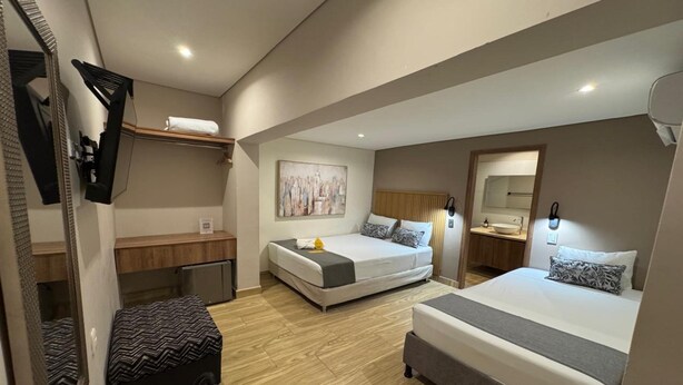 Una habitación de hotel pequeña con dos camas, un escritorio, un espejo y un cuadro en la pared.