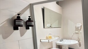 Une salle de bain moderne avec une douche à parois de verre, un lavabo blanc, un miroir et deux flacons de shampoing posés sur une étagère fixée au mur.