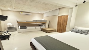 Une chambre d’hôtel moderne équipée d’un lit superposé, d’un lit simple, d’un bureau avec une lampe, d’un climatiseur et d’une armoire.