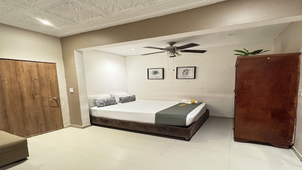 Une chambre à coucher avec un lit, un ventilateur de plafond, une armoire en bois et une porte.