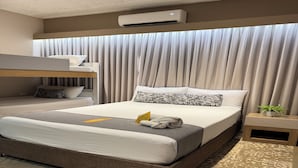 A hotel room with a bunk bed, a large bed with patterned pillows, a bedside table with a plant, and an air conditioning unit. - Habitación Múltiple Superior cerca a Getsemani (Cartagena)
