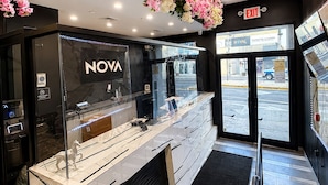 A modern interior with a reception desk, a glass display case, and a ceiling adorned with flowers. - Nova Hotel JFK (Jamaica)