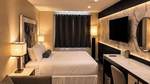 Habitación de hotel con cama, mesita de noche, lámpara, escritorio, silla y televisión.