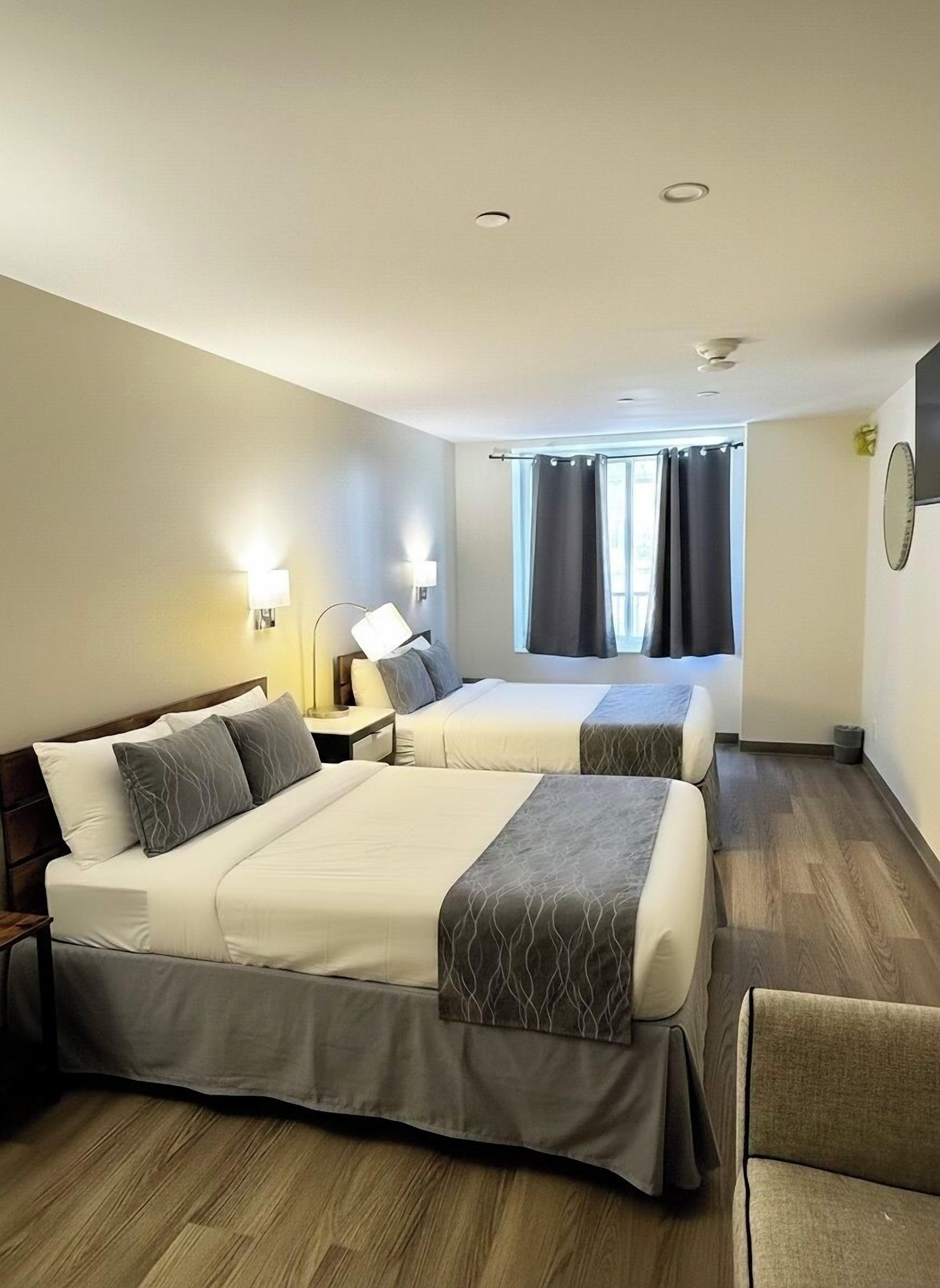 Habitación de hotel con dos camas, una ventana con cortinas, un televisor de pantalla plana y suelo de madera.