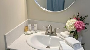 Un baño con un lavamanos blanco, un espejo redondo y un perchero para toallas.