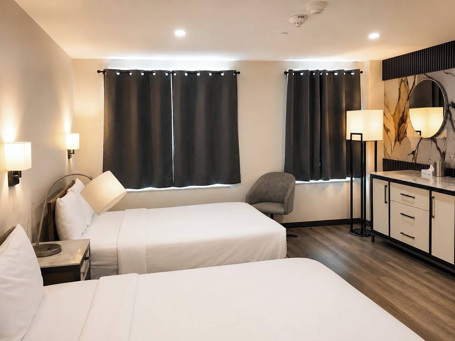 A hotel room with two beds, a desk, a chair, a dresser, and a large mirror.