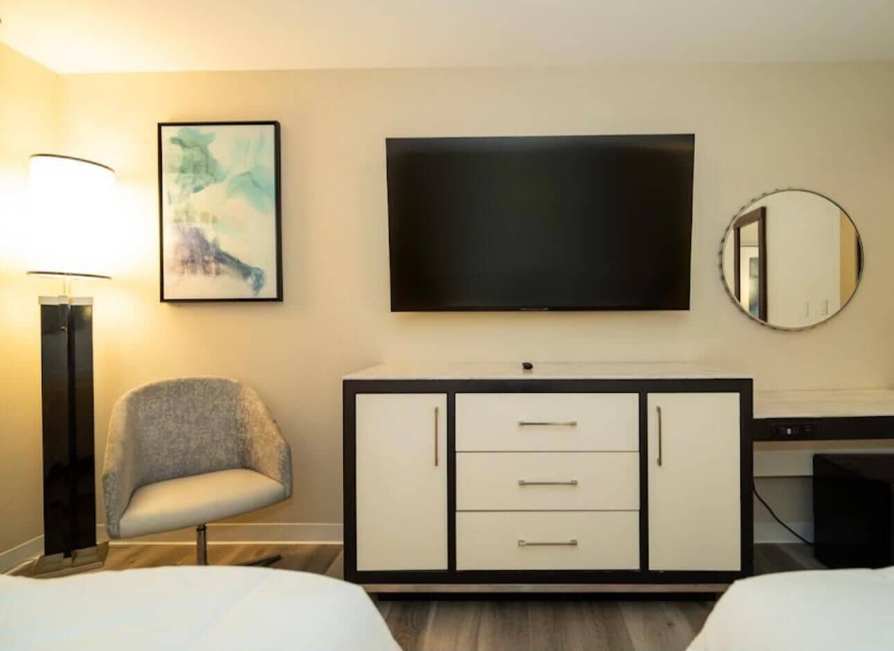 Habitación de hotel con cama, escritorio, silla, televisor, lámpara y armario.
