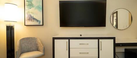 A hotel room with a bed, a desk, a chair, a TV, a lamp, and a cabinet.