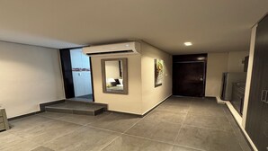Un pasillo moderno con unidad de aire acondicionado integrada, un pequeño rincón de descanso con espejo y una puerta oscura al final.