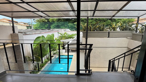 Un espacio al aire libre techado con piscina, escaleras y vegetación circundante.