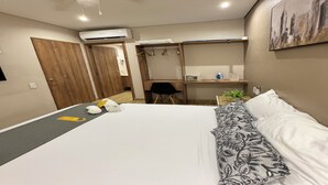 Una habitación de hotel con cama, escritorio, silla, armario y unidad de aire acondicionado.