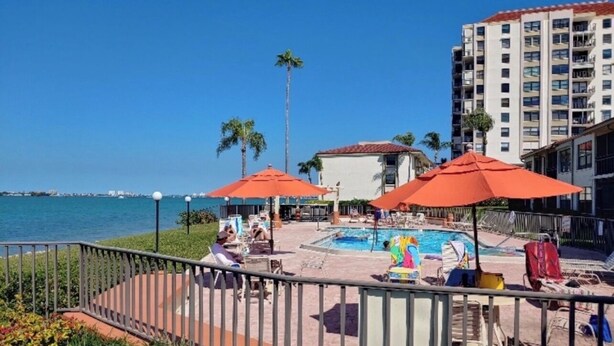 A pool area with umbrellas, lounge chairs, and a view of the ocean. - Charming condo in fantastic St. Petersburg Beach, with waterfront, sunset views (St. Petersburg)