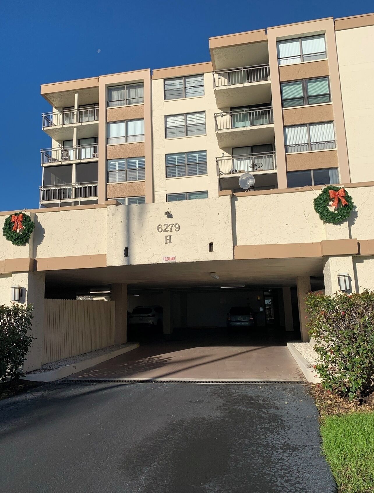 Un edificio residencial de varios pisos con entrada a un estacionamiento, número 6279 H, y coronas navideñas en las paredes exteriores.