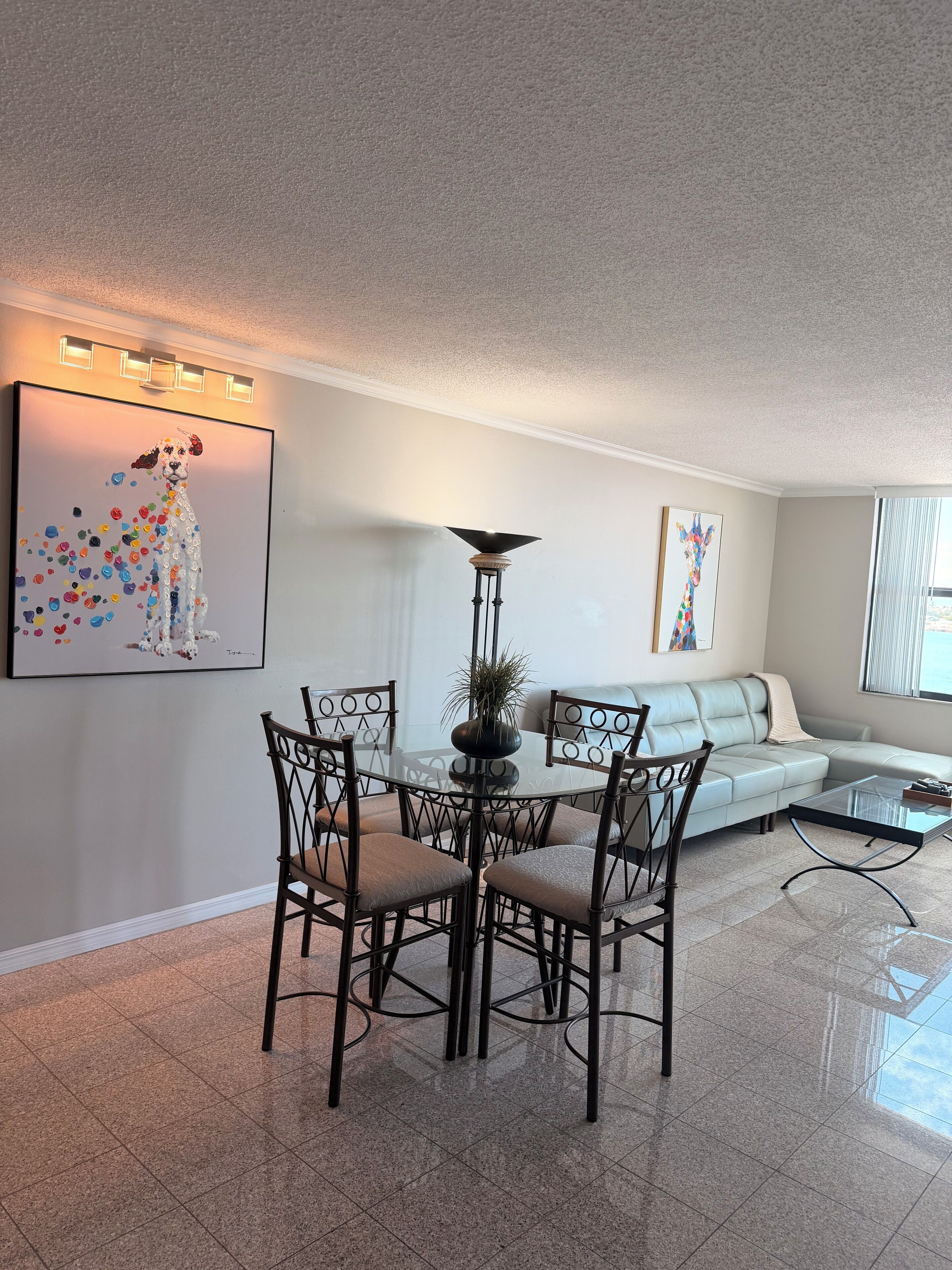 A dining area with a glass table and chairs, a floor lamp, and artwork on the walls.