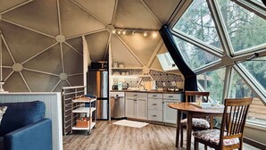 A cozy interior with a dining area, kitchen, and a large window offering a view of trees.