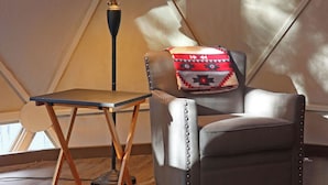 A cozy room with a sloped ceiling, a lamp, a cushioned chair, and a small table.