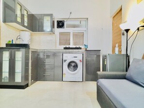Una cocina compacta con lavadora, armarios grises y un sofá gris.