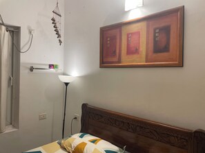 Una camera da letto con testiera in legno, un letto con copripiumino decorato, una cornice appesa al muro, una lampada da terra e un elemento decorativo a parete.