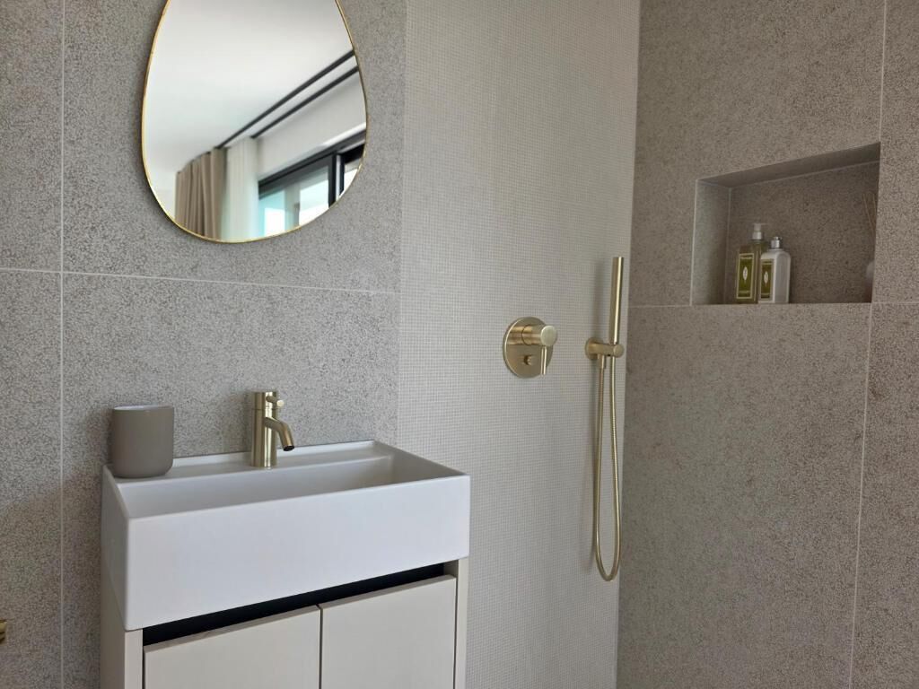 A modern bathroom with a white vanity, a gold faucet, a mirror, and a shower area with a towel rack.