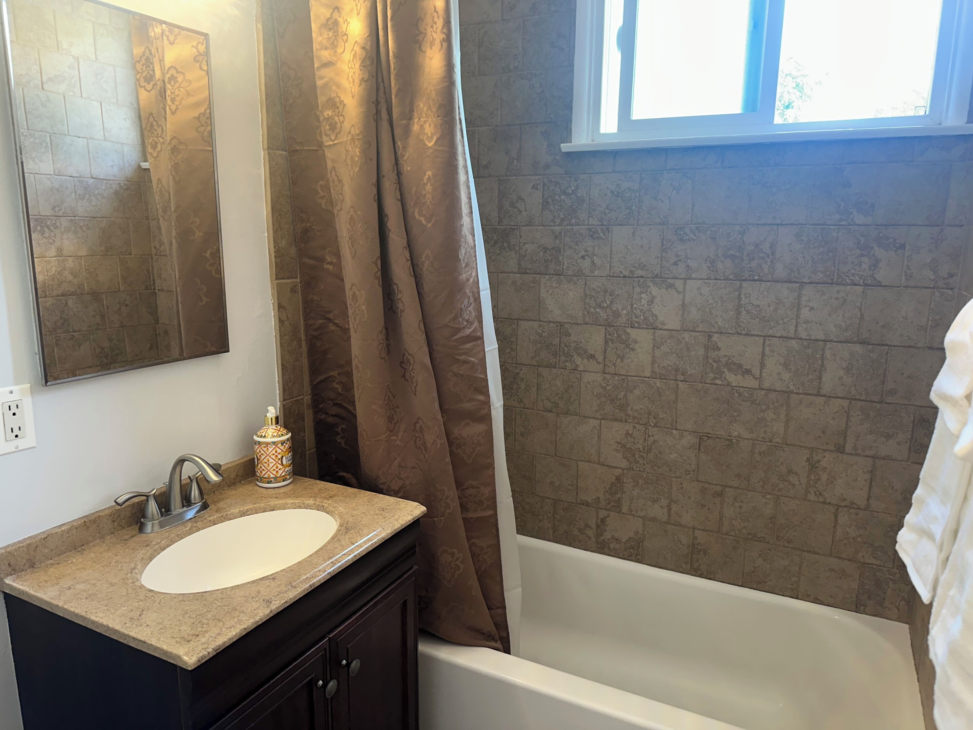 Ein Badezimmer mit einer weißen Badewanne, einem beige gefärbten Waschbecken mit einer Dekorationsschale und einer Duschvorhang mit floralem Muster.