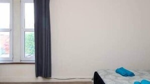 Una habitación con una cama, un ventanal con cortinas y un enchufe a la vista.