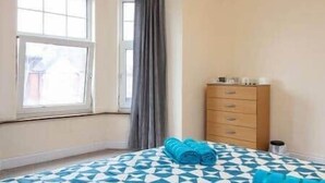 Een slaapkamer met een bed met een decoratieve spreidek, een houten dressoir en een raam met gordijnen.