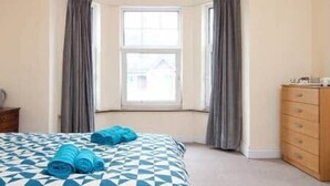 Een hotelkamer met een geruite sprei, een houten dressoir en een raam met gordijnen.