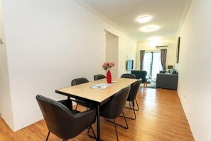 Un salón moderno con una mesa de comedor de madera, sillas negras y un jarrón rojo con flores.