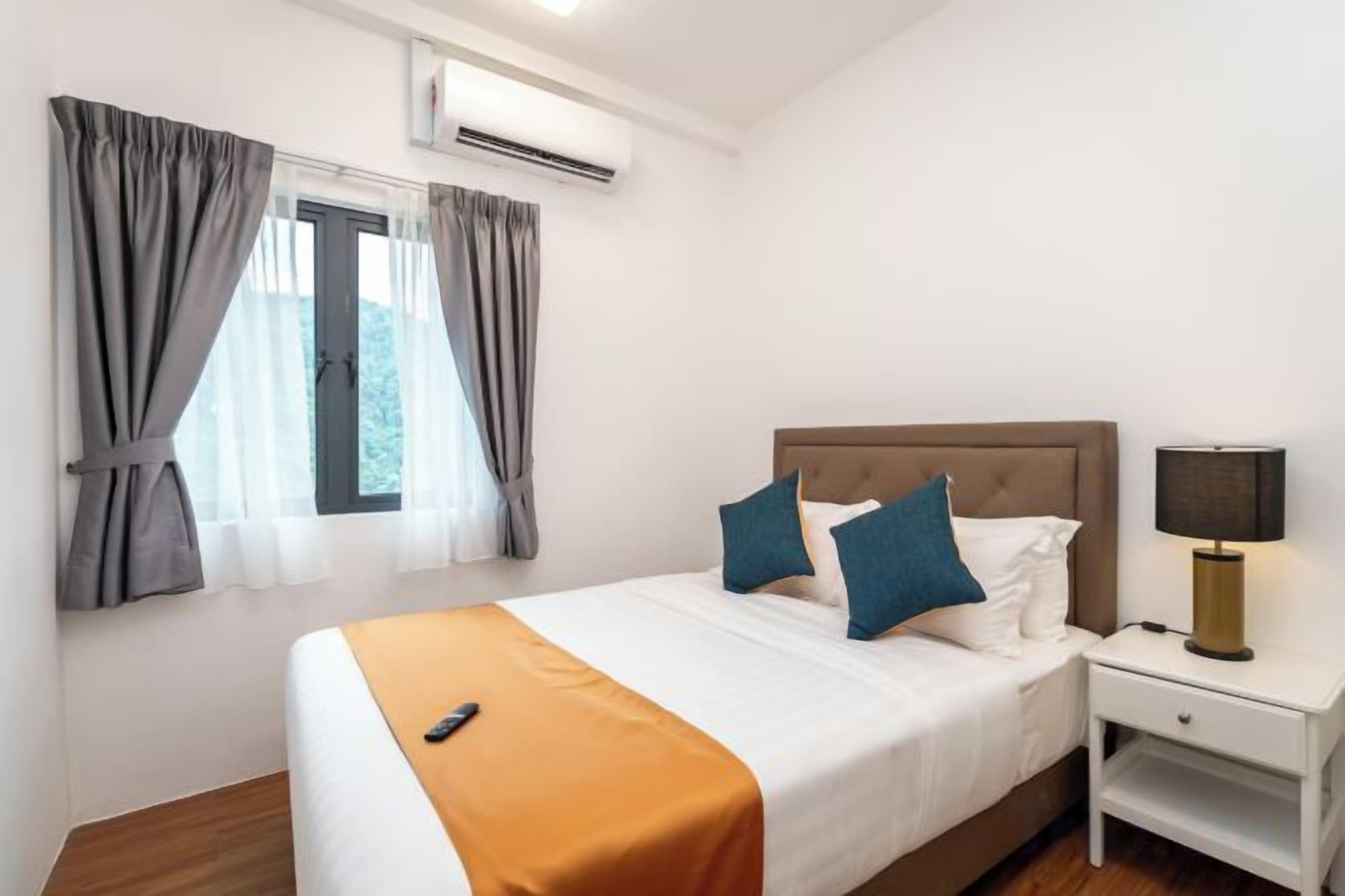A hotel room with a bed, a nightstand, a lamp, and an air conditioning unit.