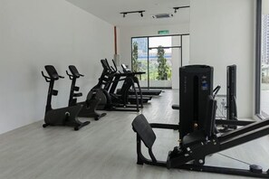 Un gimnasio con diversas máquinas de ejercicio, un ventanal con vistas y una puerta con letrero de salida.