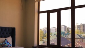 Una habitación de hotel con una cama grande, vista a la ciudad a través de una ventana y una lámpara de techo moderna.