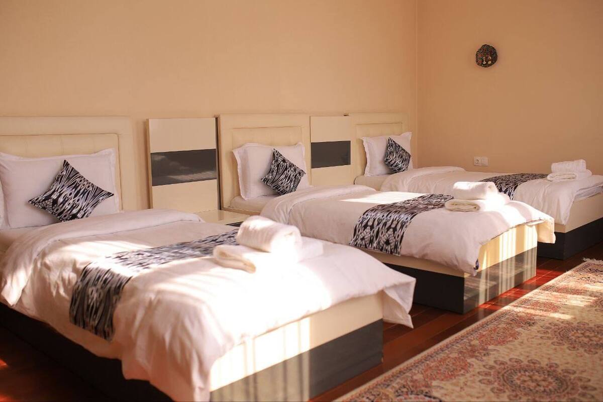 Ein Hotelzimmer mit drei Betten, jeweils mit Kopfteil, weißer Bettwäsche und Zierkissen.