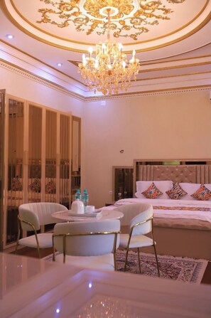 Una camera da letto lussuosa con un letto grande, un lampadario e un angolo salotto con sedie e un tavolo.